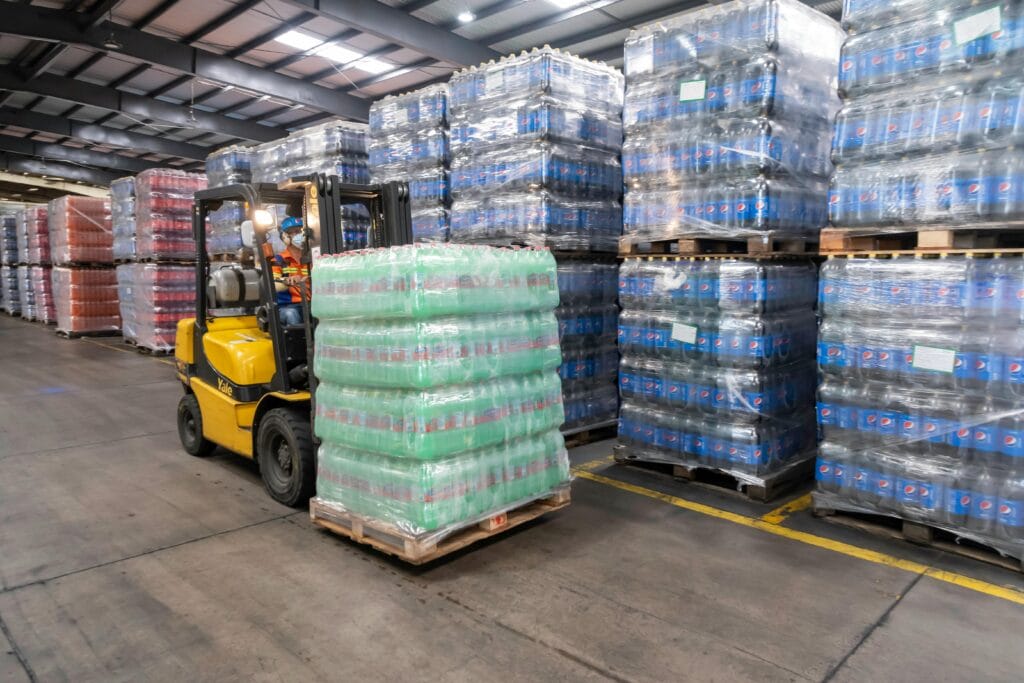 pexels-photo-17229385-17229385 A forklift operator moves stacked pallets in a busy warehouse setting.
